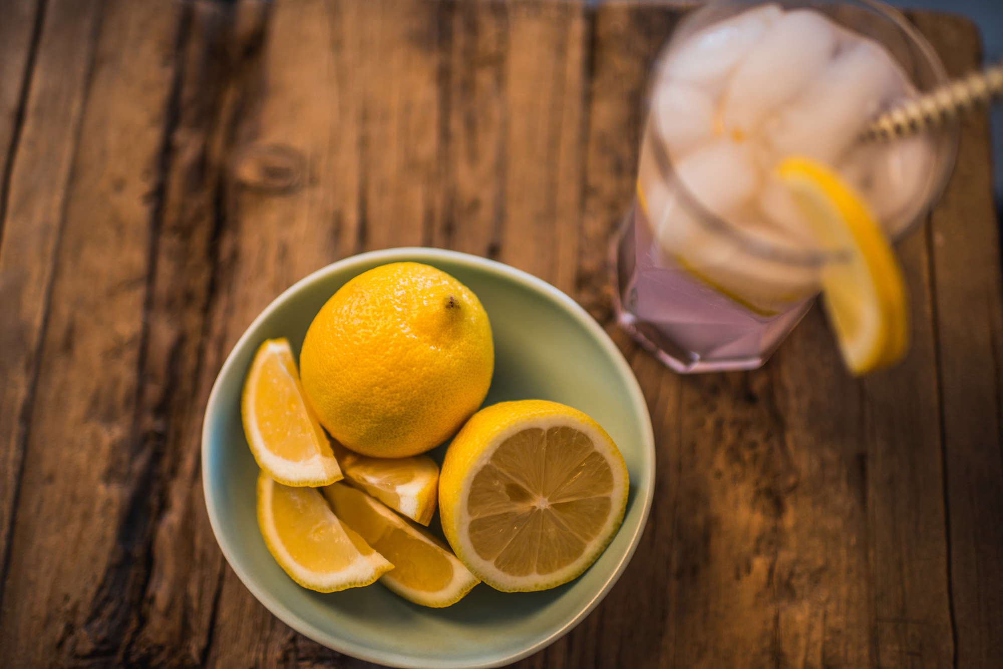 a bowl of lemons with a glass of lemonade beside it